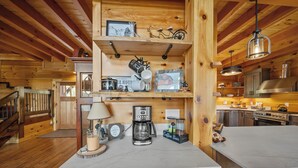 Ein Holzblockhaus-Interieur mit einer Küchenzeile, die eine Kaffeestation, einen Herd und einen Esstisch zeigt.