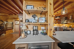 Ein Holzblockhaus-Interieur mit einer Küchenzeile, die eine Kaffeestation, einen Herd und einen Esstisch zeigt.