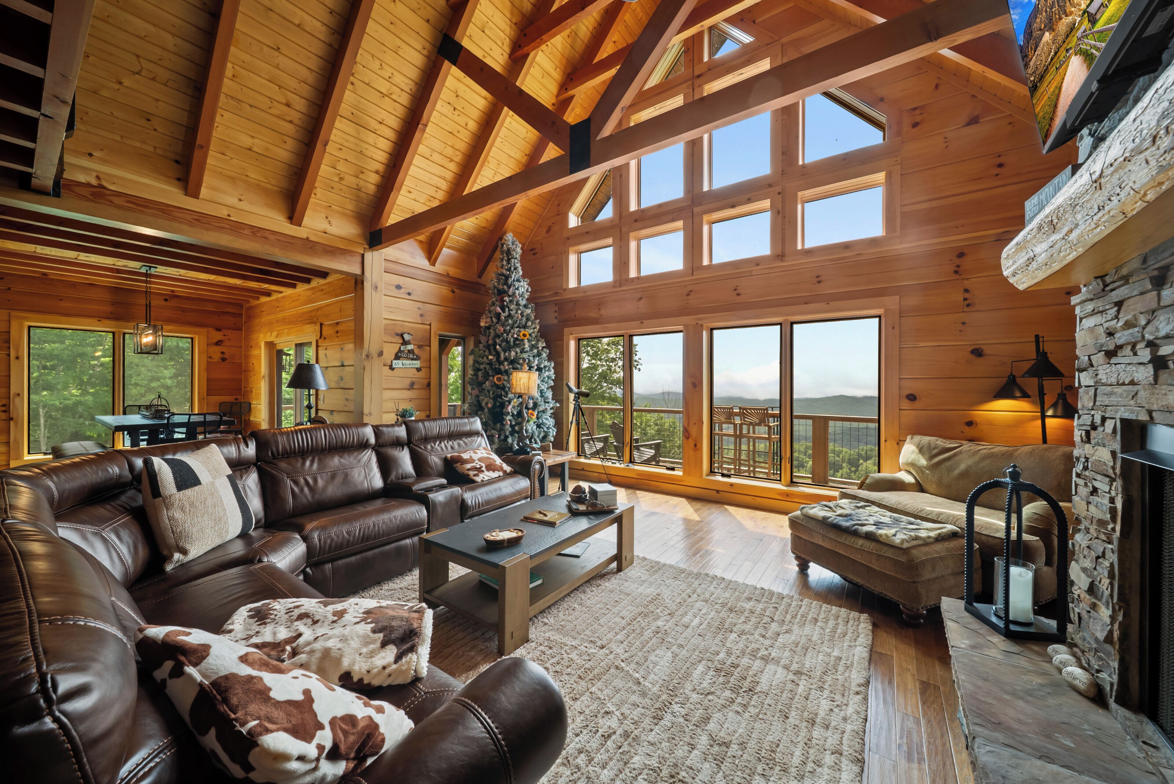 A spacious living room with a large wooden ceiling, a Christmas tree, leather sofas, and a stone fireplace.