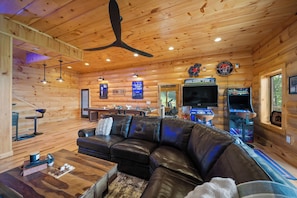 A log cabin interior with a leather couch, pool table, arcade games, and a television. - Grandfather Mountain Views, Hot Tub, Game Room & Putting Green (Seven Devils)