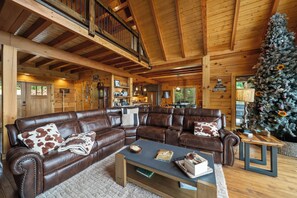 A spacious living room with a large brown leather sectional sofa, a coffee table, and a decorated Christmas tree. - Grandfather Mountain Views, Hot Tub, Game Room & Putting Green (Seven Devils)