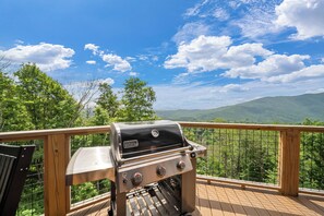 Una barbacoa damunt d'un pont de fusta amb vista a muntanyes i arbres.
