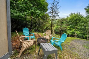 Uma área de estar ao ar livre com duas cadeiras Adirondack azuis, uma mesa pequena e uma lareira.