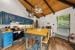 A modern kitchen with blue cabinets, a wooden dining table, and a hanging light fixture. - Cozy 2BR retreat near Beech Mountain Resort. (Beech Mountain)