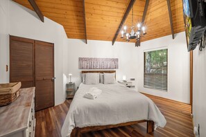 A bedroom with a wooden ceiling, a bed with white bedding, a nightstand, a wall-mounted TV, and a window with blinds. - Cozy 2BR retreat near Beech Mountain Resort. (Beech Mountain)