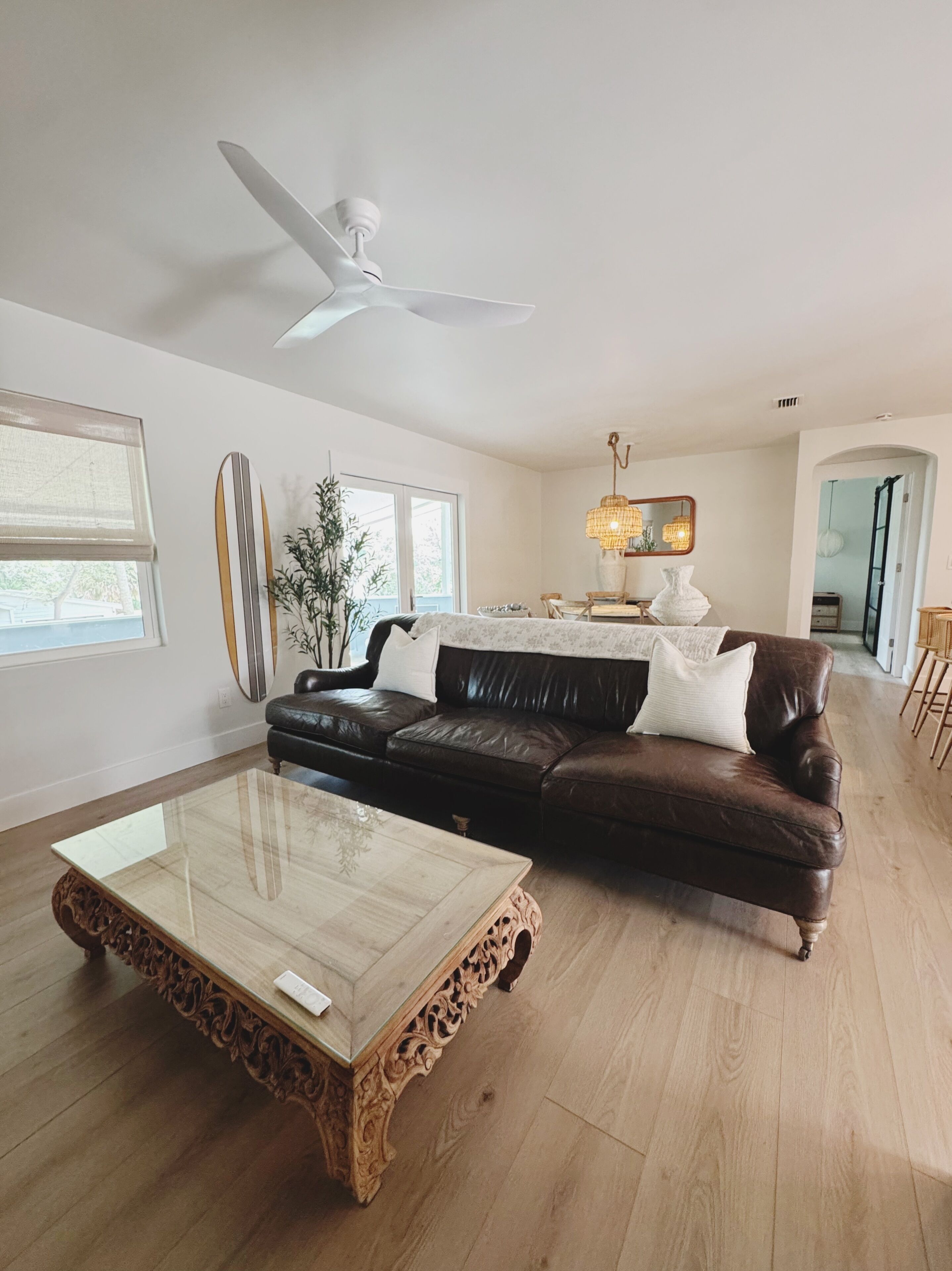 A modern living room with a glass coffee table, a leather sofa, and a ceiling fan.