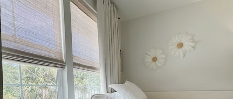 Habitación de hotel con dos camas, ventana con vista a palmeras y una pared decorada con dos motivos florales blancos.