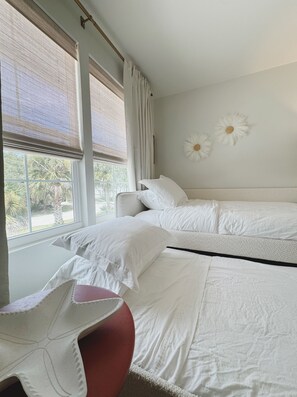 A hotel room with two beds, a window with a view of palm trees, and a wall with two white flower decorations. - Sunset Retreat | 3BD 2BA (St. Augustine)