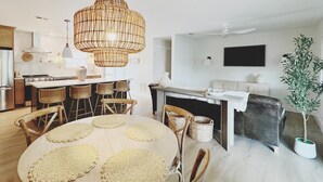 Ett modernt kök med en köksö i mitten, en matplats med ett runt bord och ett vardagsrum med en soffa och en tv.