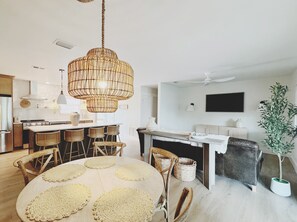 Eine moderne Küche mit Kochinsel, ein Essbereich mit rundem Tisch und ein Wohnzimmer mit Sofa und Fernseher.