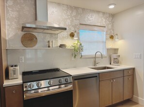 A modern kitchen with a gas stove, oven, dishwasher, and a window with blinds. - Sunset Retreat | 3BD 2BA (St. Augustine)