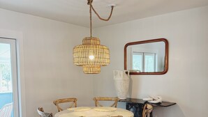 En matplats med ett runt bord, fyra stolar, en hängande lampa, en spegel och en vas på ett avlastningsbord.
