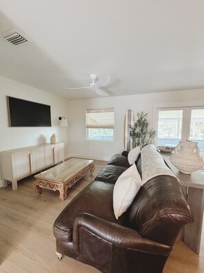 Ein Wohnzimmer mit braunem Ledersofa, einem Holztisch, einem weißen Schrank und einem Deckenventilator.