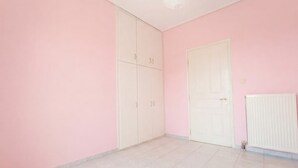 Una habitación con paredes rosas, un armario blanco, una puerta blanca y un radiador blanco.