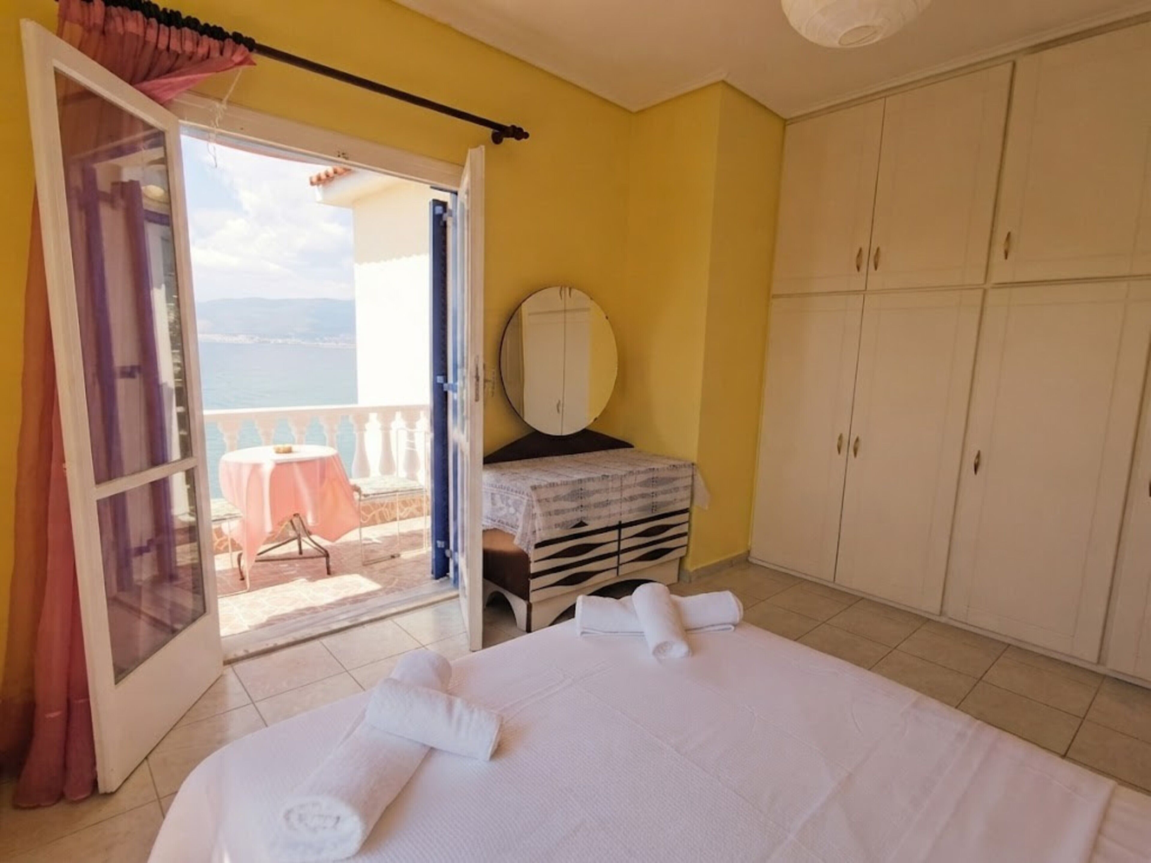 Une chambre à coucher avec un lit, une petite table, une armoire et une vue sur la mer par une porte ouverte.