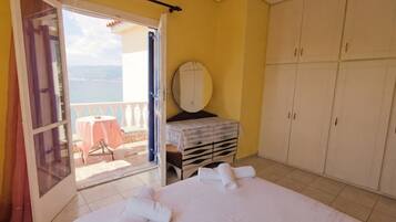 Une chambre à coucher avec un lit, une petite table, une armoire et une vue sur la mer par une porte ouverte.