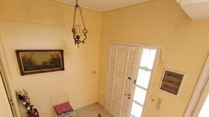 Un pasillo con puerta, un cuadro, un jarrón y una silla.
