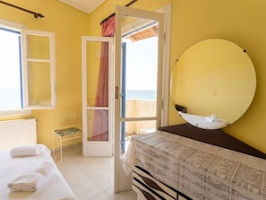 A room with a bed, a bedside table, a mirror, a window, and a door leading to a balcony.