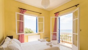 Un dormitorio con cama, ventana con cortinas, balcón con vistas y una puerta.