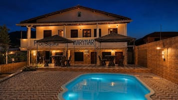 Hotel com piscina, área de estar externa e fachada bem iluminada.