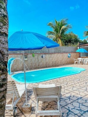 Piscina con sillones de descanso y sombrillas, rodeada de un patio de piedra y palmeras.