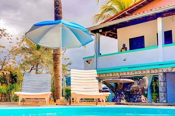 A pool area with lounge chairs, a palm tree, and a building with a balcony.