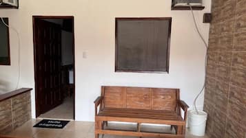 Una habitación con un banco de madera, una puerta, un aire acondicionado instalado en la pared y un balde blanco.