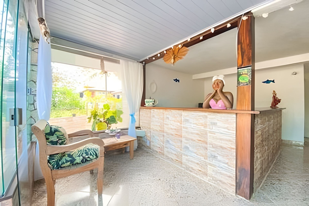 A reception area with a wooden counter, a receptionist, and a view of greenery outside.