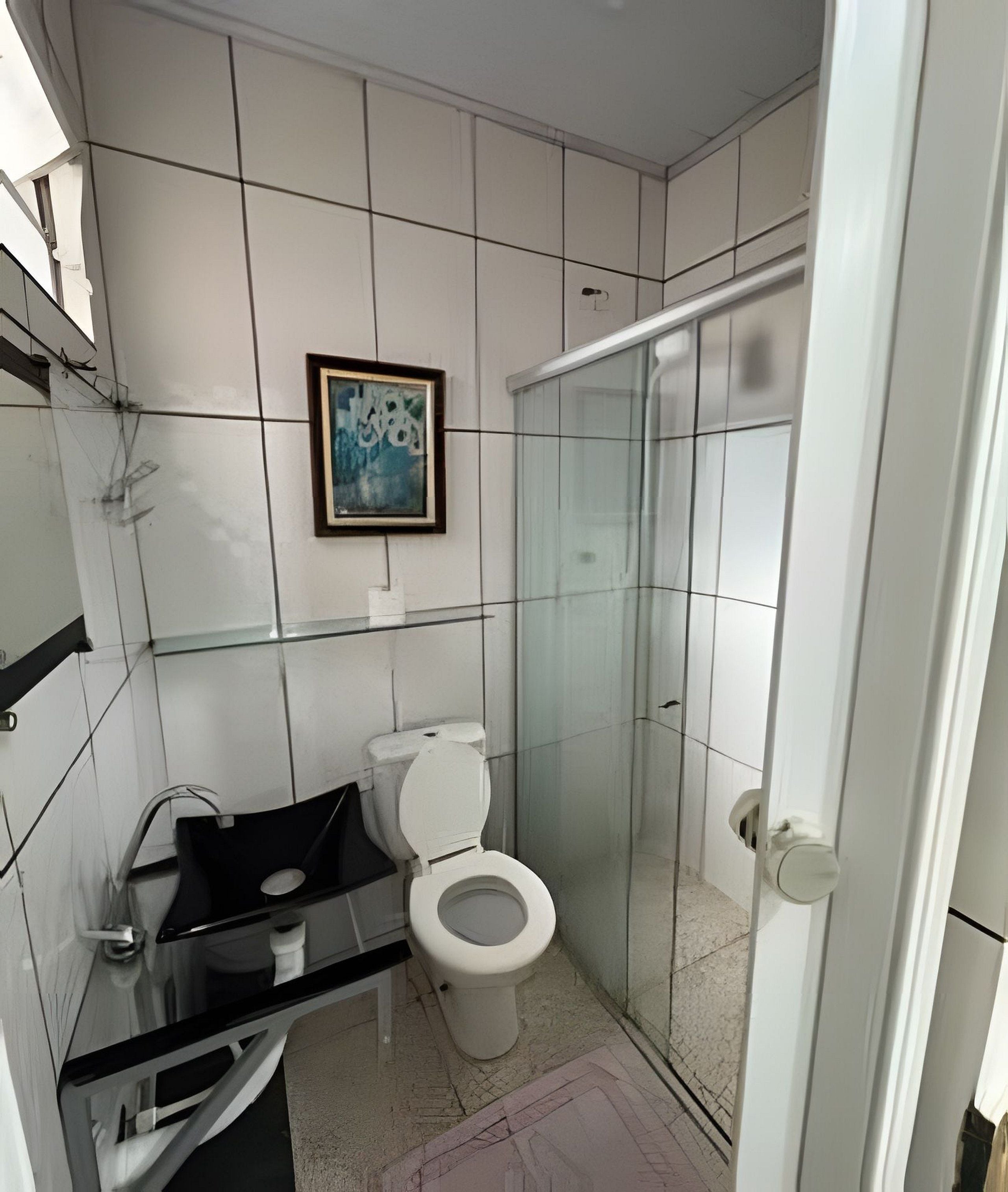 Casa de banho com sanita, cabine de duche em vidro e lavatório com bancada preta.