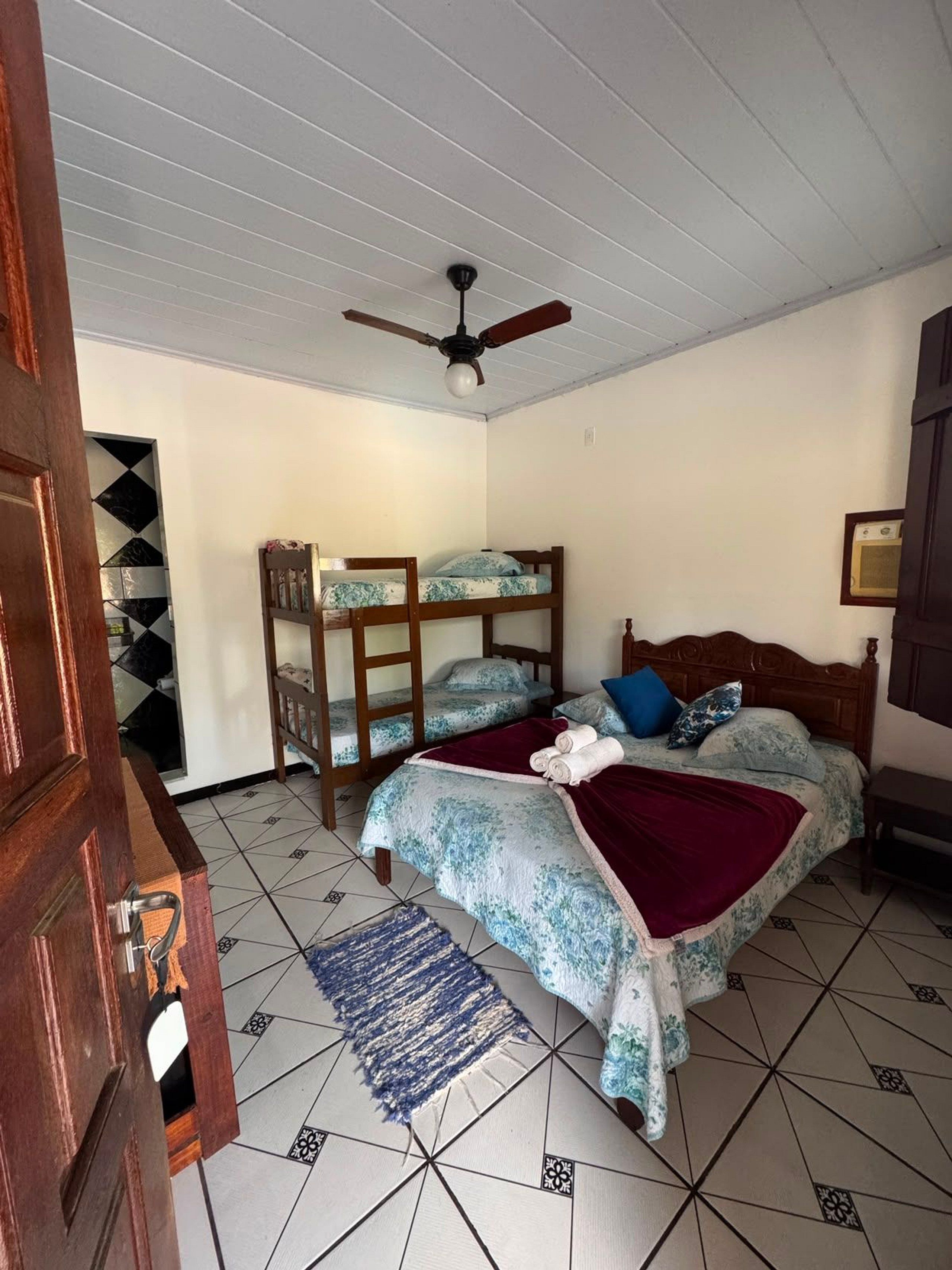 A bedroom with a bunk bed, a single bed, a ceiling fan, and a tiled floor.