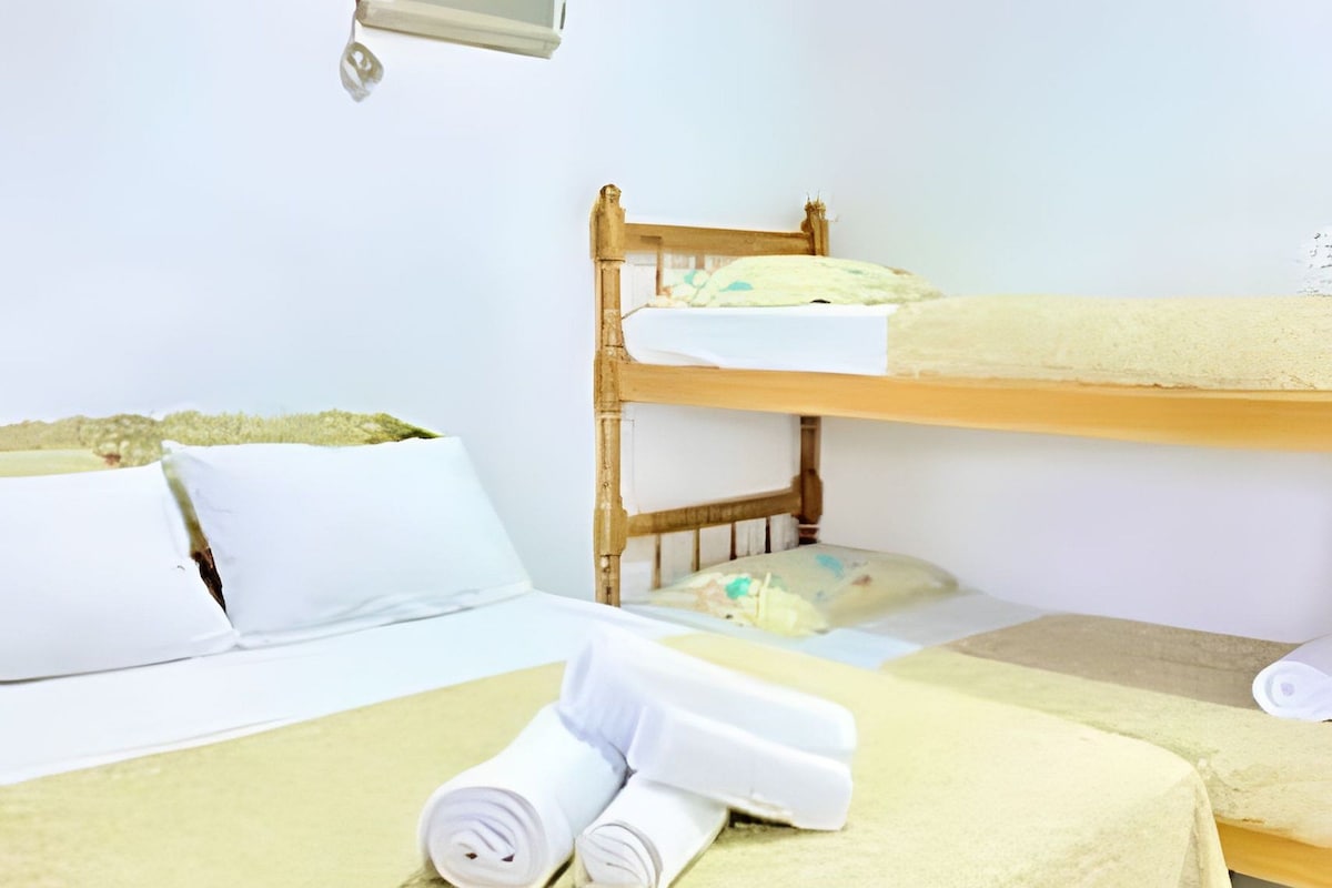 A hotel room with a bunk bed, a bed with a white duvet, and a bedside table with a lamp.