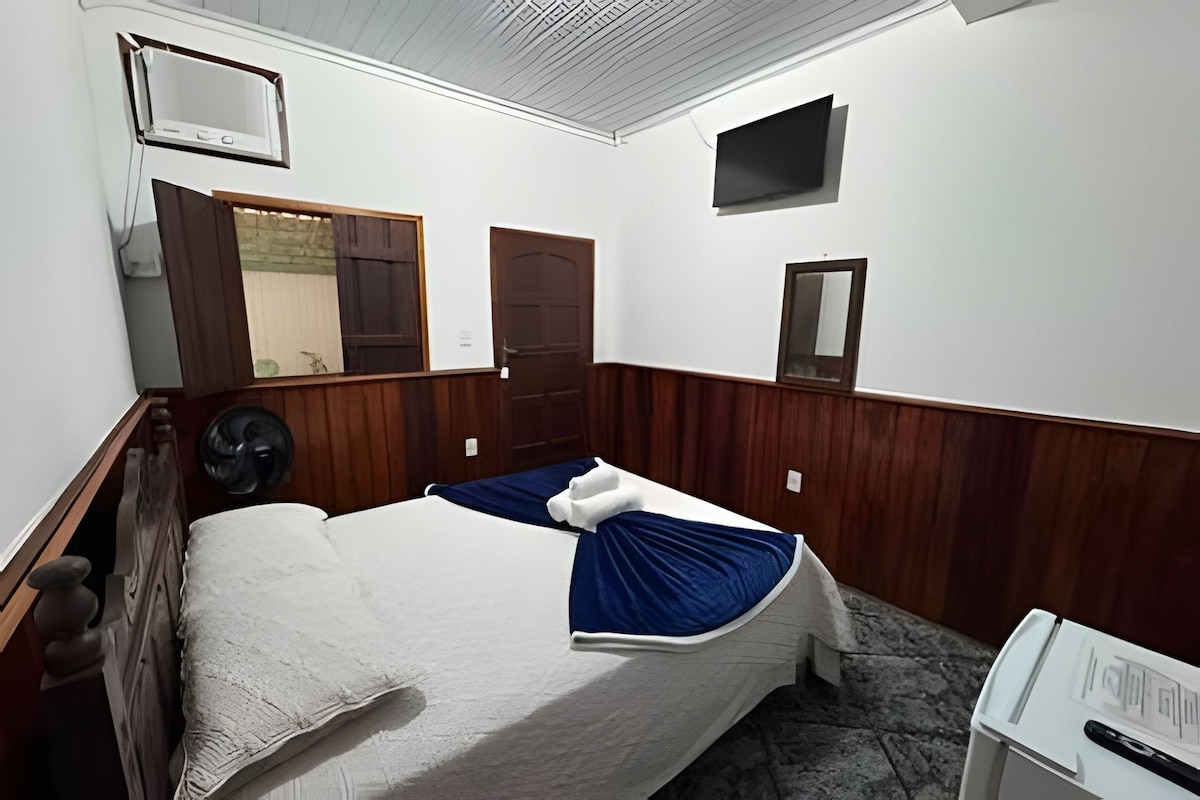 A room with a bed, a fan, a television, and a door.