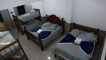 Quarto com três beliches, uma cadeira de madeira e uma mesa pequena.