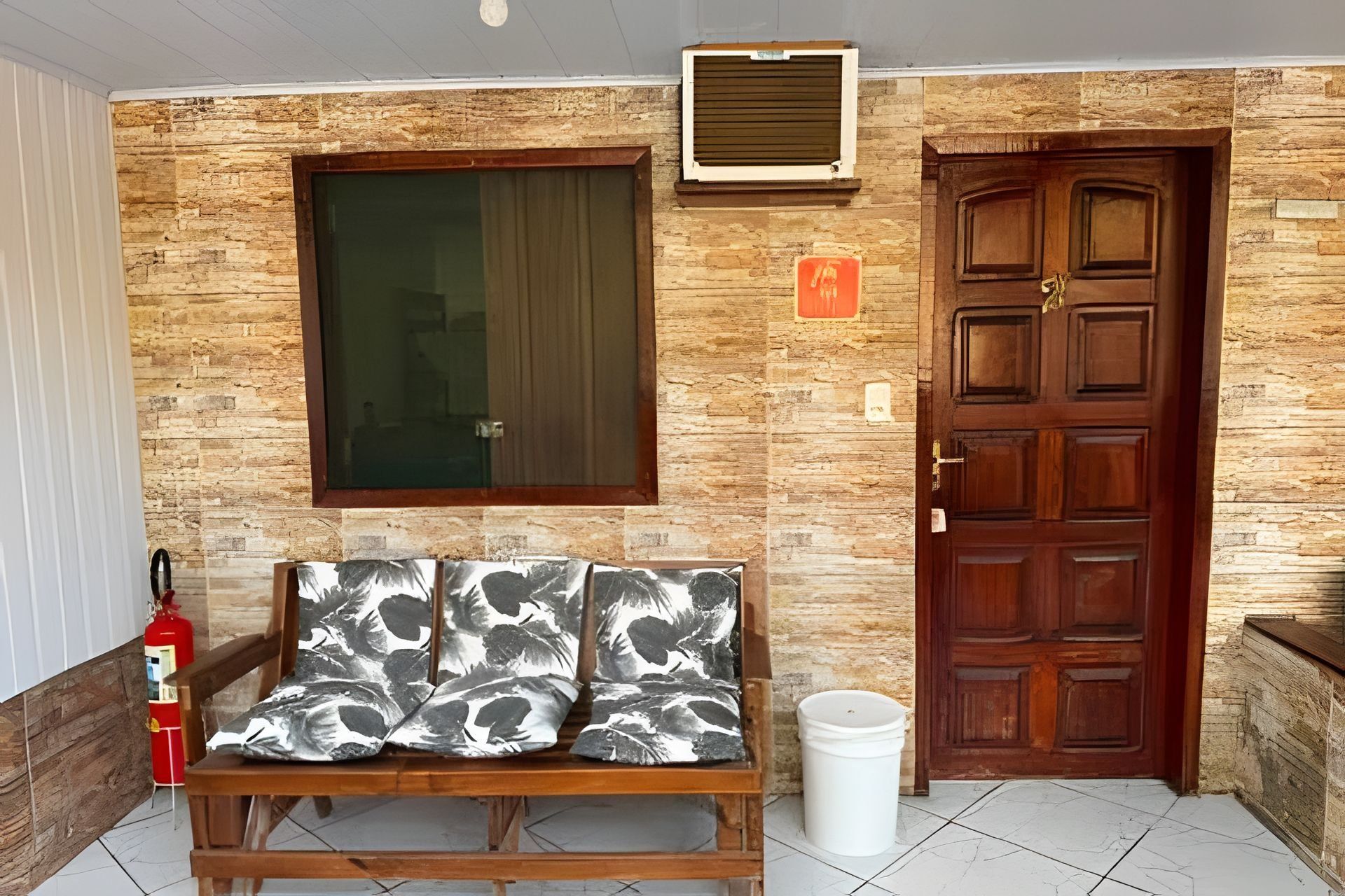 A room with a wooden bench, a fire extinguisher, a window, a door, and a wall-mounted air conditioning unit.