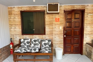 Una habitación con un banco de madera, un extintor, una ventana, una puerta y un equipo de aire acondicionado instalado en la pared.