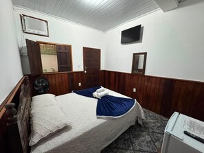 Una habitación con cama, televisión, ventilador y refrigerador.