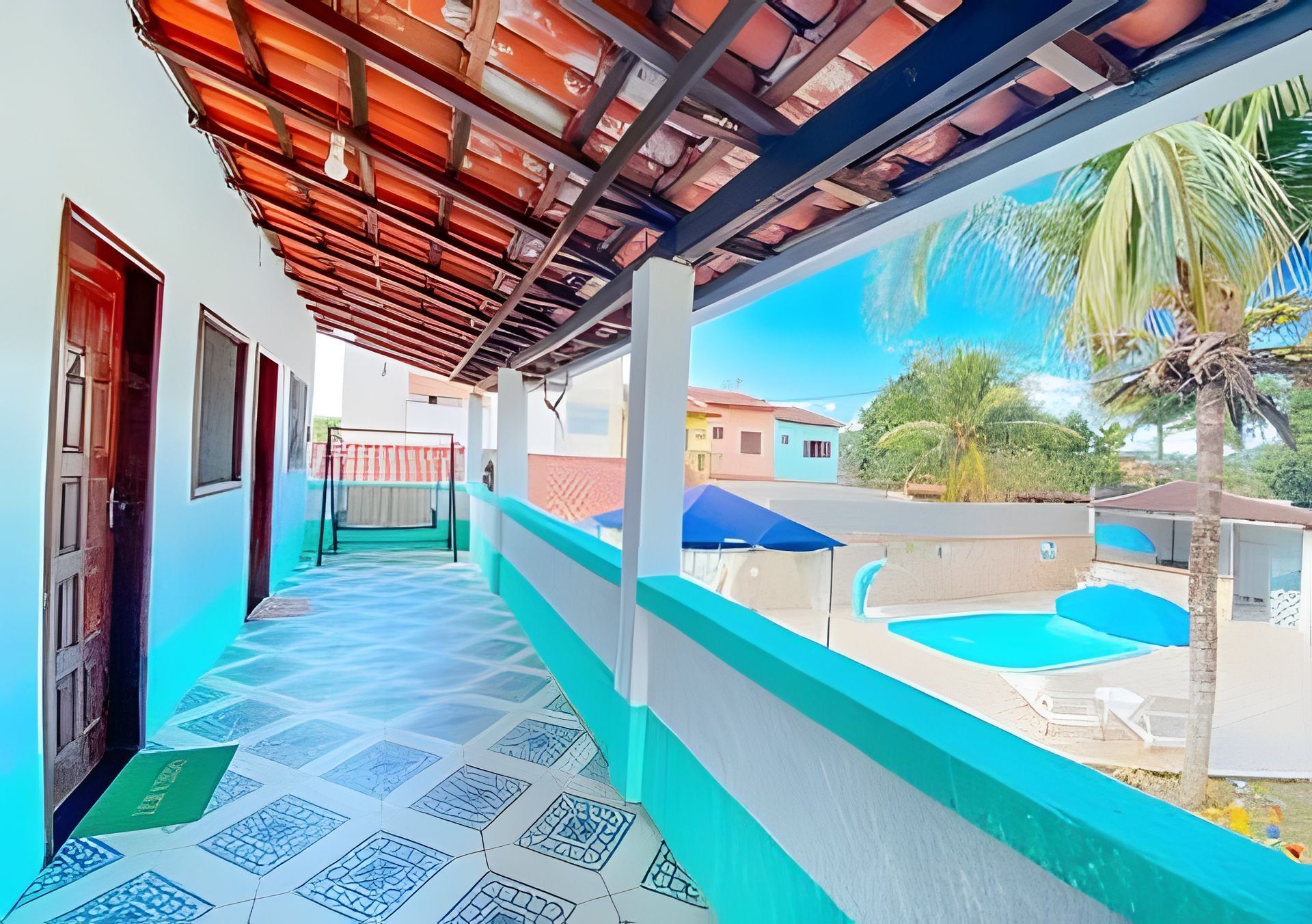 Un paseo techado que conduce a una zona de piscina con vistas a casas vecinas y una palmera.