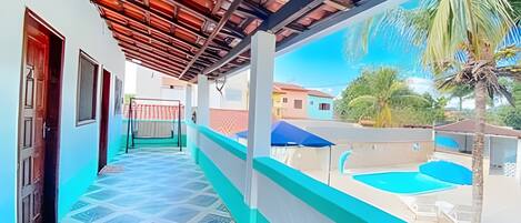 Un paseo techado que conduce a una zona de piscina con vistas a casas vecinas y una palmera.