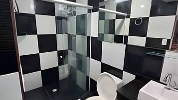 Un baño moderno con un estampado de baldosas blancas y negras en damero, un inodoro blanco, un box de ducha de vidrio y un lavabo con espejo.