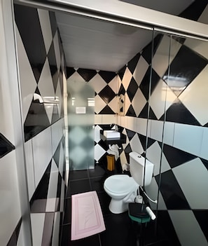 A bathroom with a modern design, featuring black and white geometric tiles, a white toilet, and a sink with a mirror.