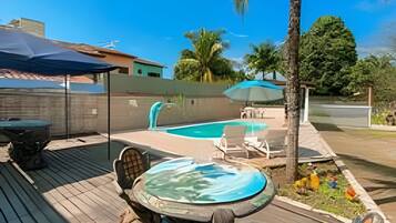 Um deck de madeira com hidromassagem, piscina e espreguiçadeiras.