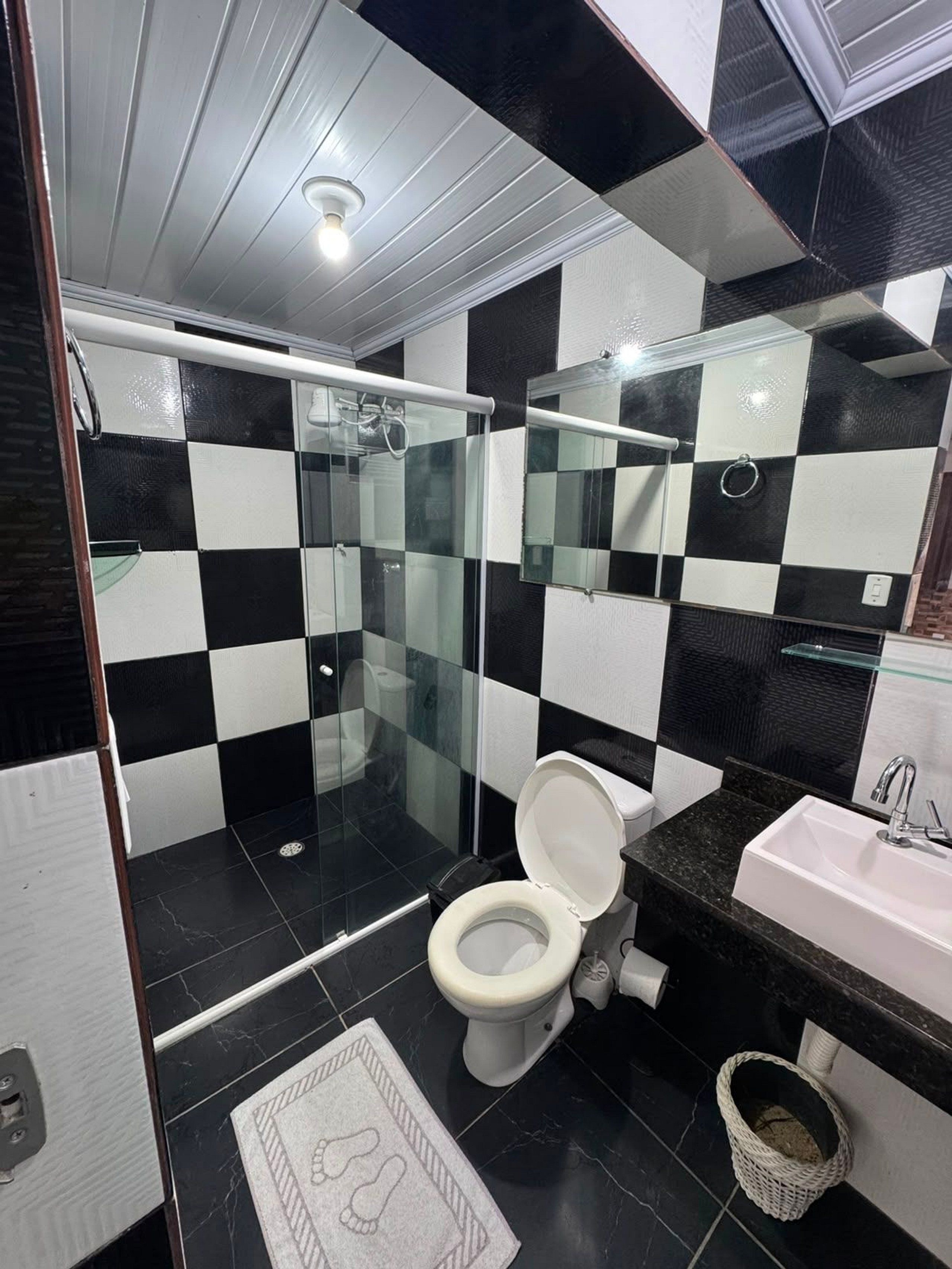 A modern bathroom with a checkered black and white tile pattern, a glass shower enclosure, a white toilet, and a sink with a marble countertop.