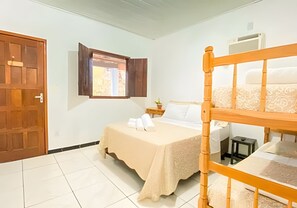 A bedroom with a bunk bed, a bedside table with a lamp, a window with curtains, and a door.