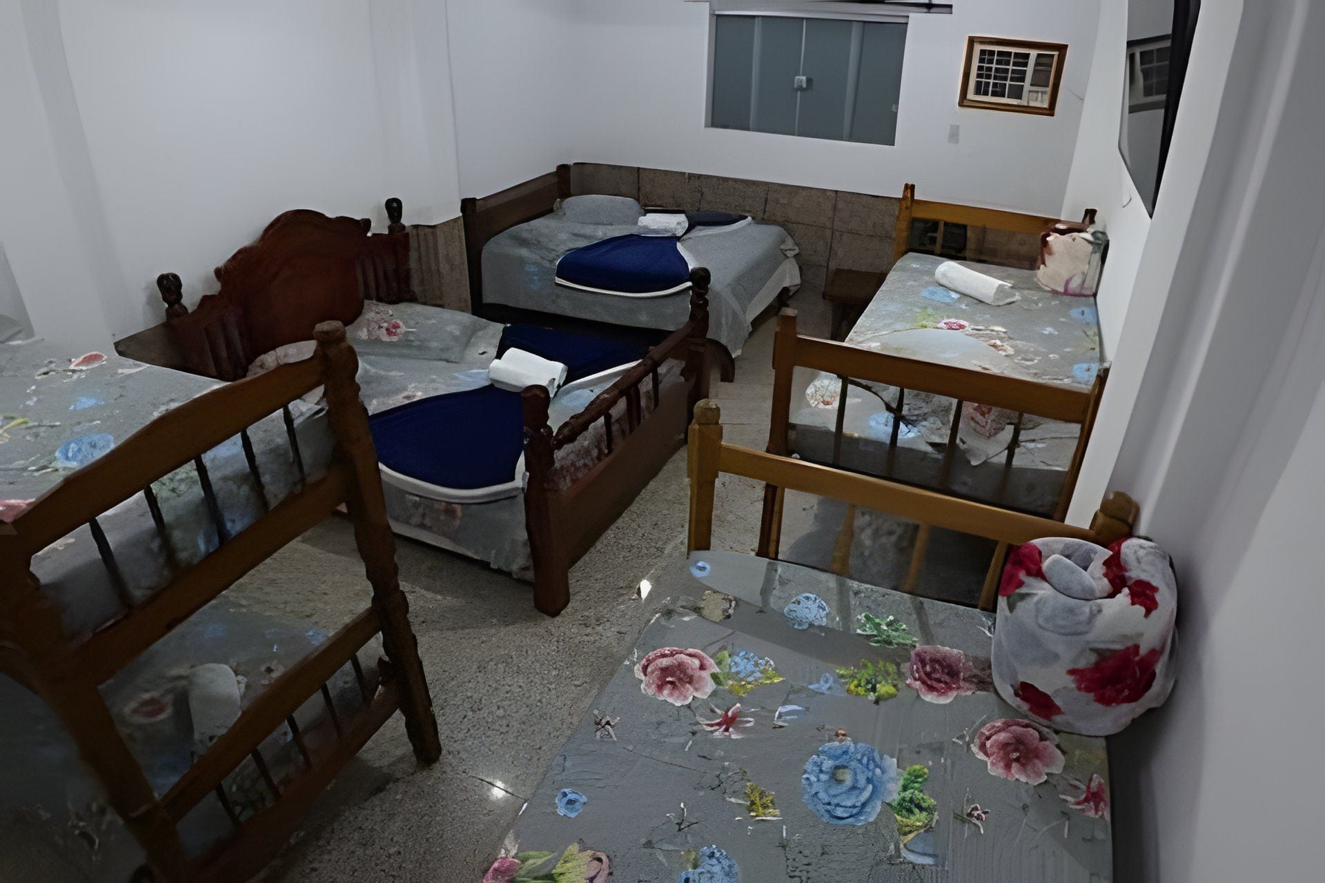 A small, compact room with three wooden beds, each with a different colored bedspread.