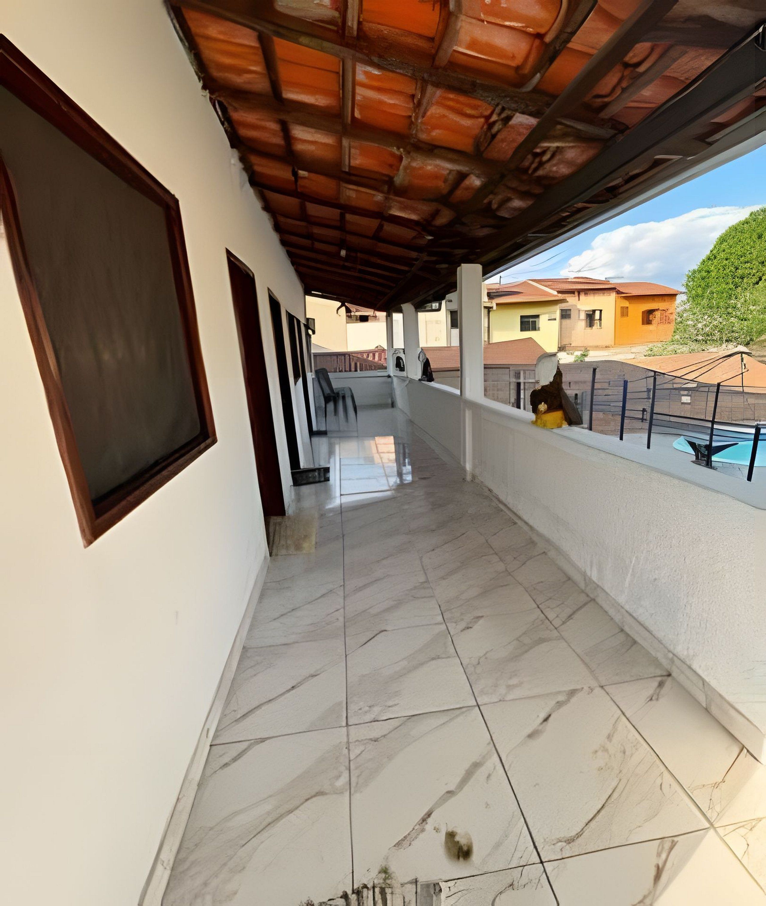 A covered balcony with a tiled floor, a view of neighboring buildings, and a clear sky.