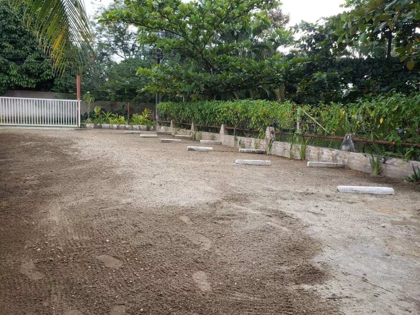 Área externa com piso de cascalho, jardineiras de concreto e cerca de metal.