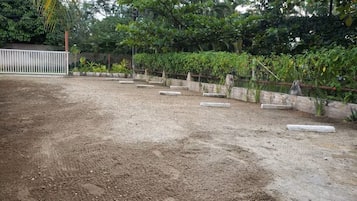 Área externa com piso de cascalho, jardineiras de concreto e cerca de metal.