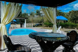 A covered outdoor area with a swimming pool, a table, and chairs.