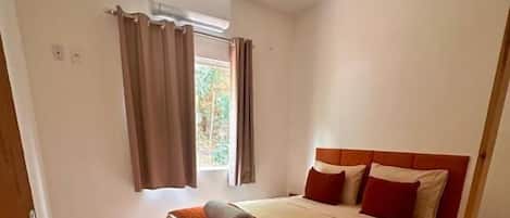 A bedroom with a bed, a ceiling fan, a window with curtains, and a wooden chair.