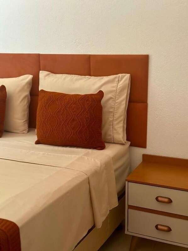Habitación de hotel con cama, dos almohadas, una mesita de noche y un cajón.
